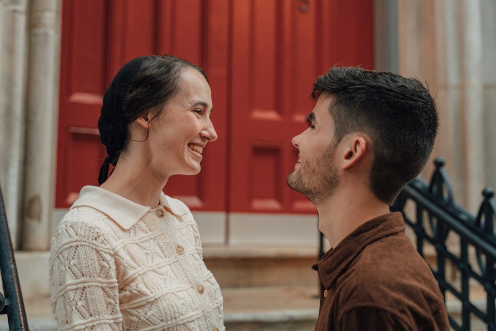 Trennis and Maria facing one another in front of a red door