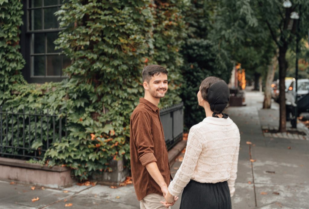 Trennis and Maria holding hands and looking back along a leafy street
